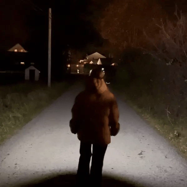Femme de dos en promenade nocturne éclairant un chemin avec sa lampe frontale Lumora