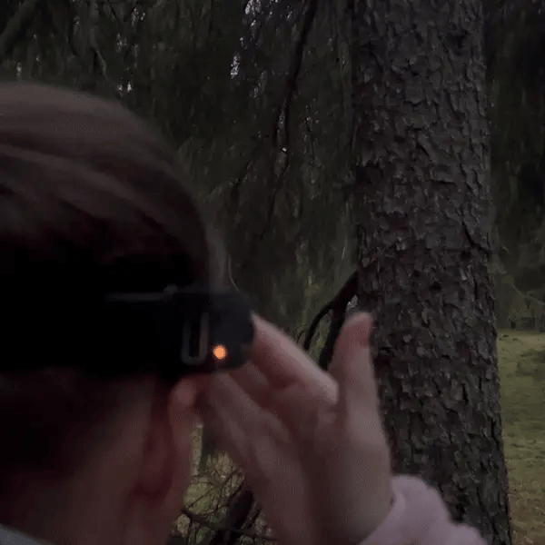 Femme activant une lampe frontale Lumora avec le détecteur de mouvement en forêt