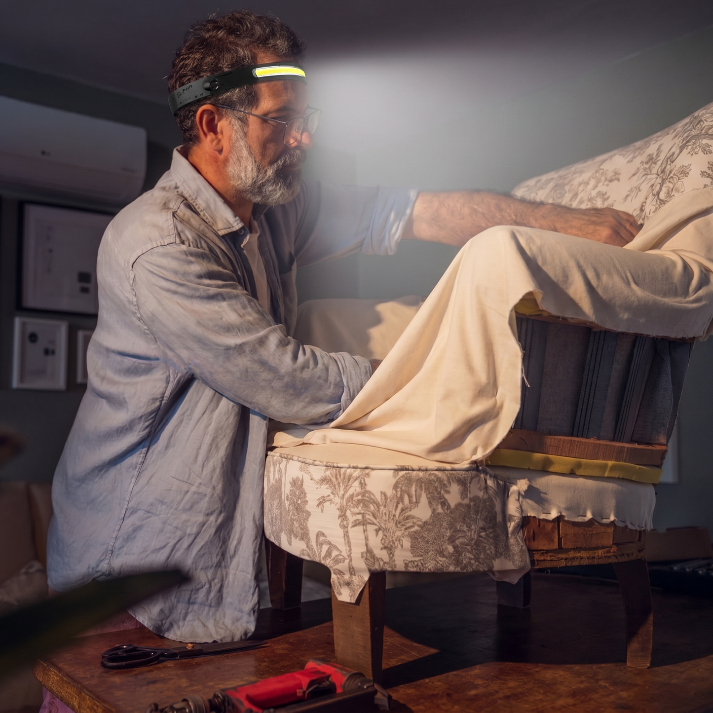 Artisan tapissier restaurant un fauteuil avec la lampe frontale Lumora pour un travail précis
